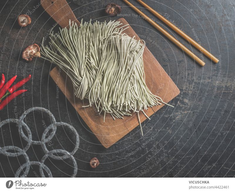 Rohe hausgemachte asiatische Nudeln auf dunklem Küchentisch mit Stäbchen. Ansicht von oben roh selbstgemacht dunkel Tisch Essstäbchen Draufsicht