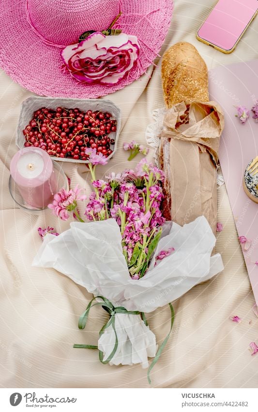 Rosa Hut mit Baguette, Blumenstrauß und Obst auf Picknickdecke. Ansicht von oben. Draußen. rosa Haufen Früchte Decke Draufsicht im Freien außerhalb Tischwäsche