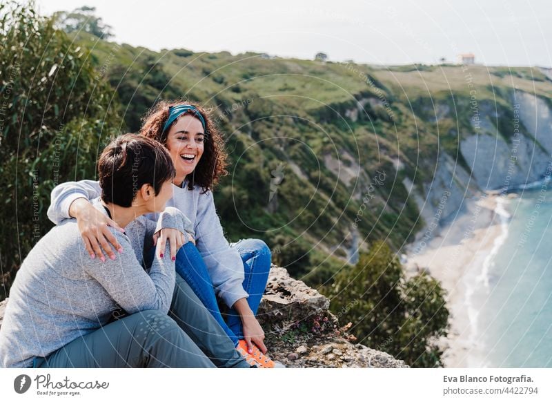 zwei Frauen Freunde sitzen, lachen und Blick auf schöne Meer Landschaft auf der Spitze des Berges. Freundschaft und Natur Konzept Paar Klippe Kaukasier 30s jung