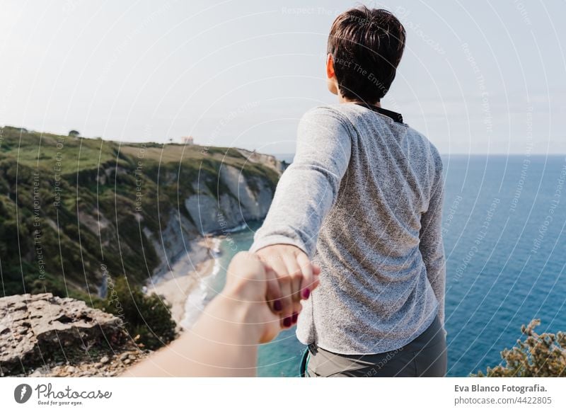 Rückenansicht der Freundin hält Hand des Freundes während der Wanderung auf der Spitze auf der Klippe. Blick aufs Meer. Entspannen und Natur Konzept Frau