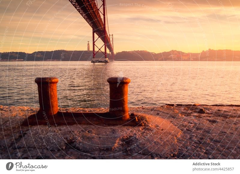 Vertäuungsmasten unter der Brücke bei Sonnenuntergang Mast Maure Fluss Ufer Himmel wolkig Wasser Konstruktion Lissabon Portugal 25 de abril brücke Tagus-Fluss