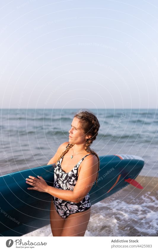 Frau mit Paddleboard am Meer Zusatzplatine SUP Paddelbrett Surfer MEER Sommer Badeanzug Surfbrett Ufer Wasser stehen Urlaub Badebekleidung Holzplatte genießen