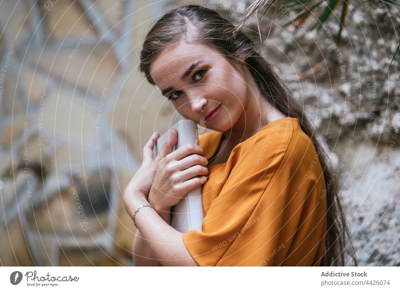 Lächelnder Schüler mit Buch in der Stadt Frau Straße Bildung Literatur klug clever jung genießen Wand lernen Glück Wissen positiv Großstadt trendy Stein