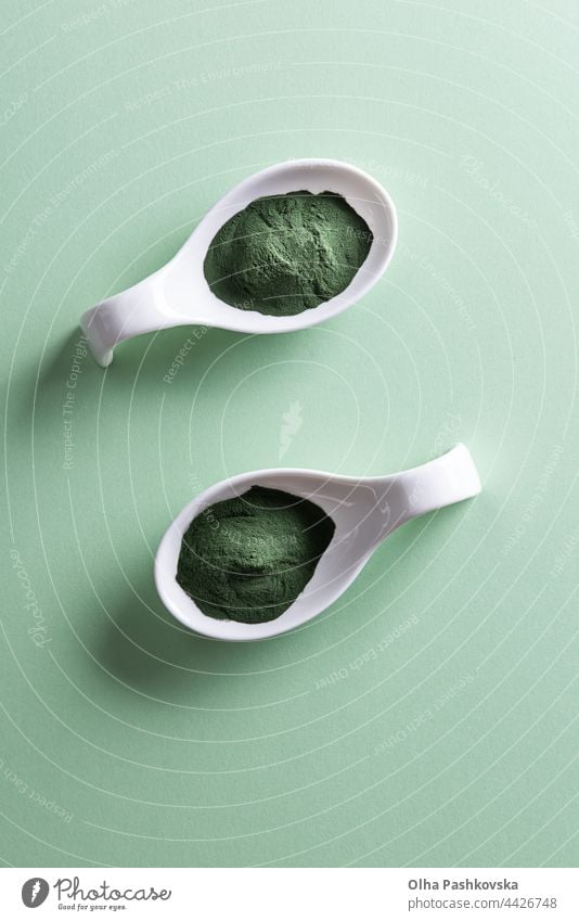 Zwei Löffel Schalen mit Chlorella- oder Spirulina-Pulver Papierhintergrund grüner Hintergrund Licht zwei Porzellan Schüsseln Form oben vertikal weiß Seegras