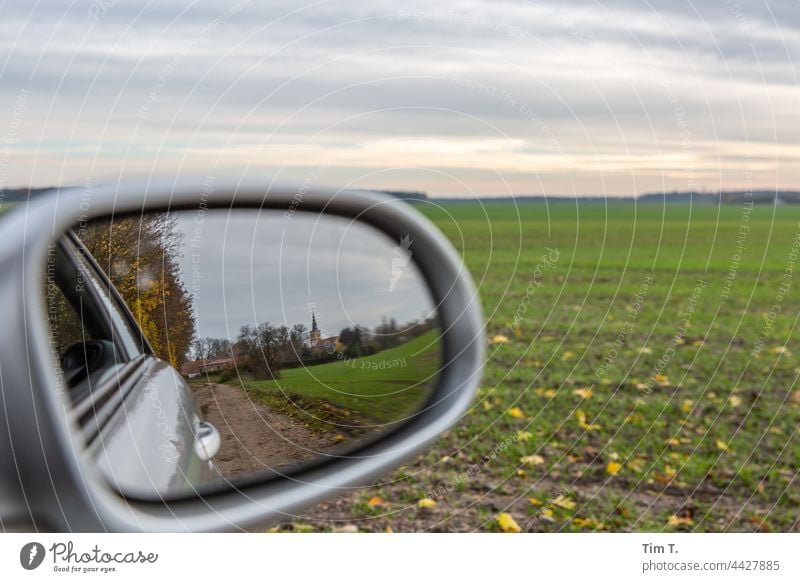 Blick in den Seitenspiegel . Man sieht ein Dorf . Autofahren Brandenburg Feld Außenaufnahme Menschenleer Farbfoto Straße Tag Landschaft Umwelt Himmel Natur