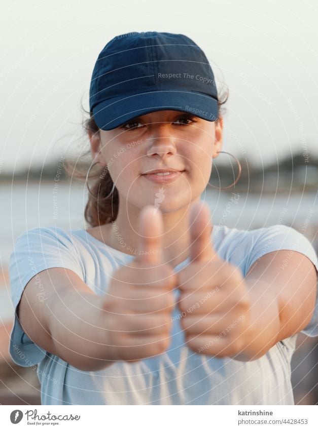 Teenager-Mädchen mit blauer Baseballmütze zeigt den Daumen hoch Sonnenuntergang Verschlussdeckel Natur Jugendlicher Attrappe Lächeln Kopfschuss MEER Kaukasier