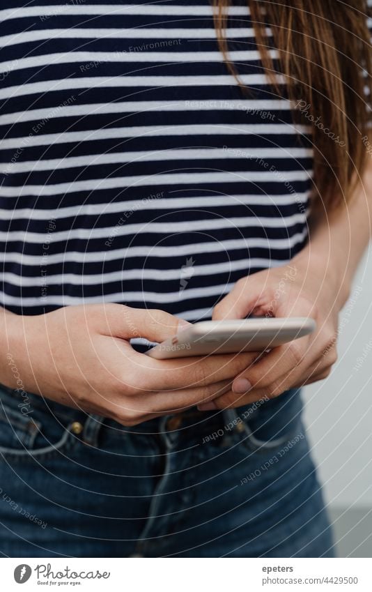 Junge Frau, die ein Smartphone in der Hand hält, nur die Hände werden gezeigt lässig Kleidung gen z Beteiligung Jeanshose gestreift streifen T-Shirt Technologie