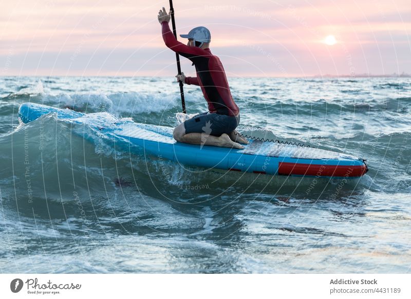 Mann mit Paddelbrett im Wasser zum Surfen Zusatzplatine Surfer Meeresufer Neoprenanzug Strand männlich Surfbrett Sport Hut Brandung MEER Seeküste Ufer