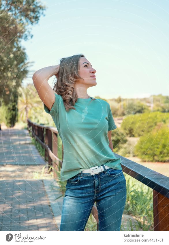 Frauen in T-Shirt und Jeans bleiben draußen im Park Erwachsener mittleres Alter Lächeln lässig Attrappe Hand über den Kopf im Freien blondhaarig Jahrtausende