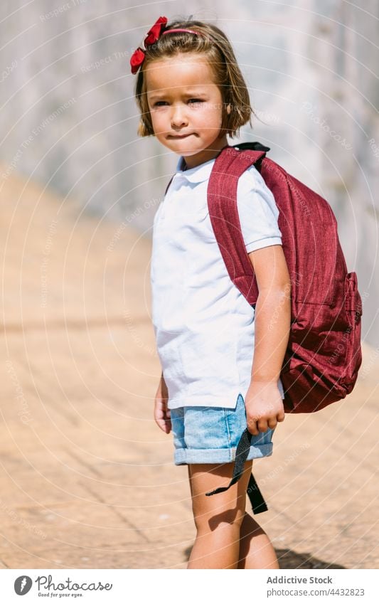 Schulmädchen in Freizeitkleidung mit Rucksack auf städtischem Gehweg neugierig Kindheit zurück zur Schule Straßenbelag Steinwand urban charmant verträumt