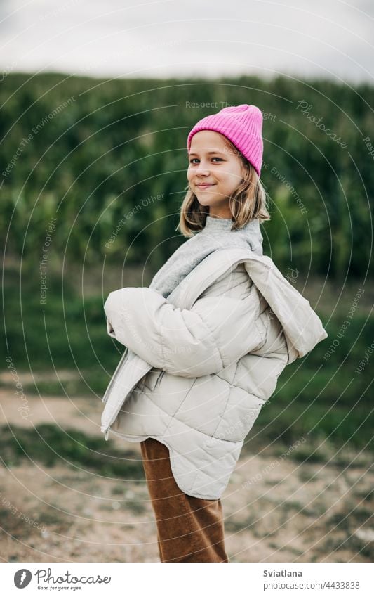 Ein Teenager-Mädchen in einem stilvollen Bild und einer rosa Mütze steht vor dem Hintergrund eines Maisfeldes Herbst gelb Kornfeld Umhang Lachen Lifestyle