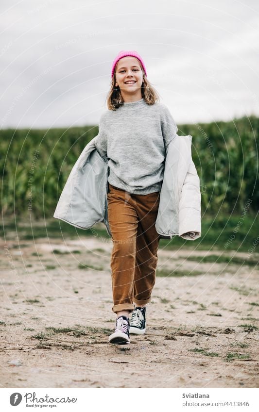 Fröhliches, hübsches Teenager-Mädchen in gelbem Regenmantel und rosa Hut läuft selbstbewusst im Maisfeld Herbst Kornfeld Umhang Lachen Lifestyle spielen