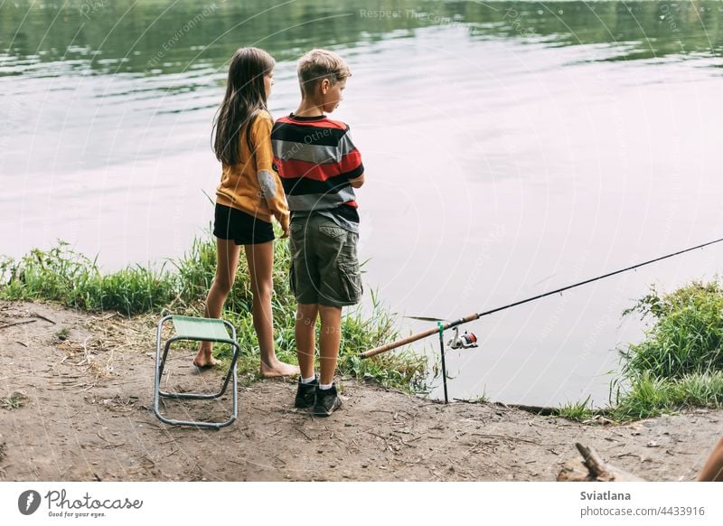 Ein Bruder und eine Schwester stehen am Flussufer und angeln während eines Familienurlaubs auf einem Campingplatz. Gemeinsame Zeit, Familienurlaub Fischen Junge