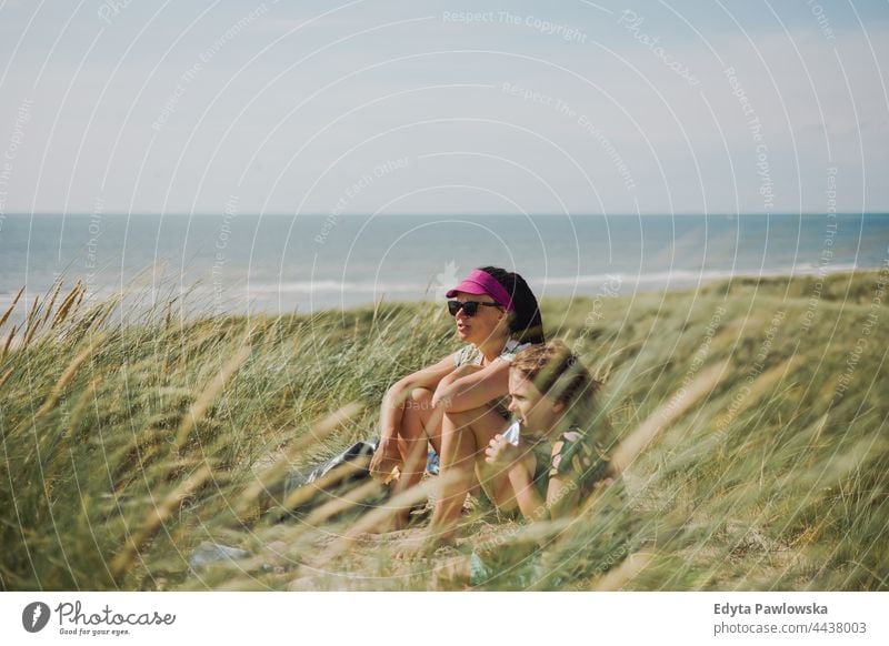 Mutter und Tochter sitzen im Gras am Meer Wildnis Feld Mama Person schön aktiv Abenteuer Strand blau Kind Kindheit Kinder niedlich Tag genießend Familie Frau