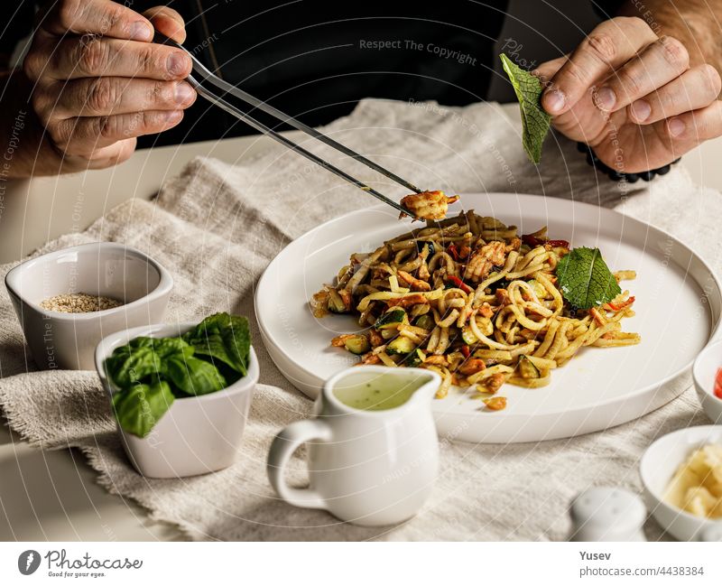 Traditionelle Nudeln mit Meeresfrüchten. Der Küchenchef bereitet eine Pasta Marinara zu. Der Chefkoch dekoriert das Gericht mit einer Pinzette. Spaghetti mit Meeresfrüchten. Mediterrane Küche. Menschen bei der Arbeit. Nahaufnahme. Körperteile