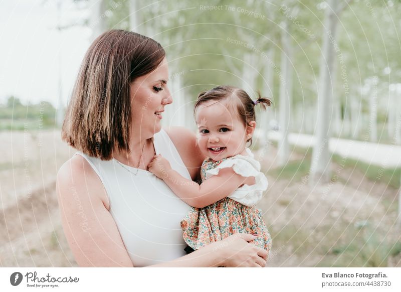 schöne Mutter hält Baby Mädchen in Bäumen Weg. Familie, Spaß und Natur Konzept Wald Glück Kindheit Lächeln laufen Kaukasier Spanien Kleid unschuldig Unschuld