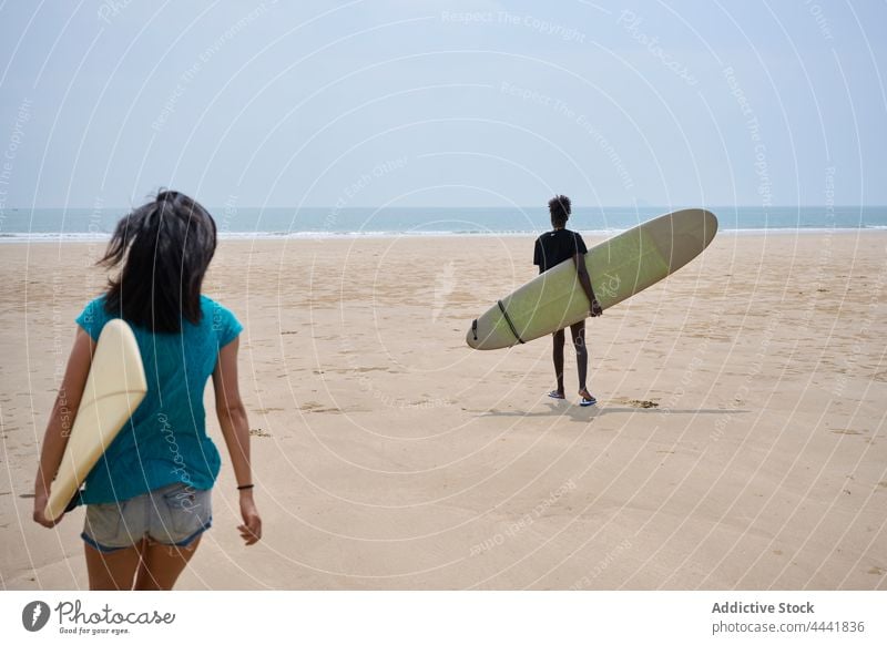 Verschiedene Sportlerinnen mit Surfbrettern unterhalten sich bei einem Spaziergang am Meer reden Freundschaft Surfen Zeit verbringen Ufer Blauer Himmel Frauen