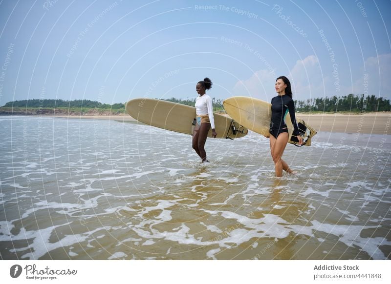 Diverse Surfer mit Surfbrettern im schäumenden Meer Sportlerinnen Surfen Longboard Zeit verbringen Körper schaumig Blauer Himmel Frauen Freundin Neoprenanzug