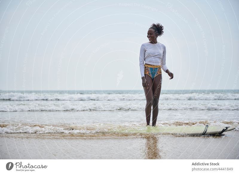 Lächelnder schwarzer Surfer am Meeresufer mit Longboard surfen MEER Sport Surfen Bikini stürmisch Himmel Frau Afroamerikaner Surfbrett Strand Natur