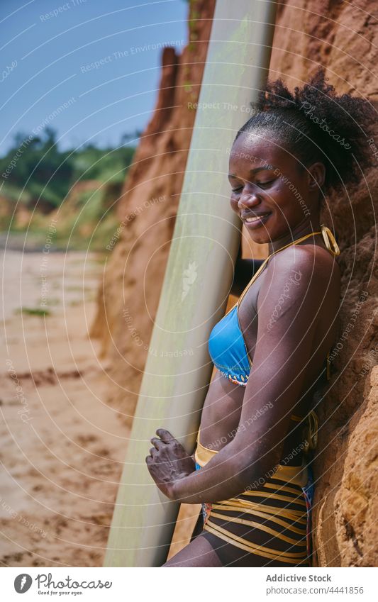 Afroamerikanischer Sportler posiert mit einem Surfbrett vor einem Tonfelsen Surfer Longboard Surfen nachdenken Strand Natur Frau Sportlerin schwarz ethnisch