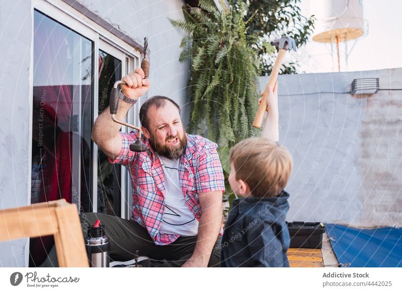 Begeisterter Vater und Sohn bei der Arbeit mit Holz Papa Holzarbeiten heiter Hammer Handarbeit diy Basteln Glück Mann Freude Zeit verbringen Lächeln Hipster