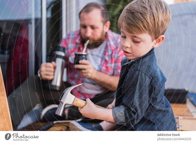 Vater trinkt Mate gegen Sohn, der mit Holz arbeitet Gefährte Thermoskanne trinken Holzarbeiten achtsam Hammer eingießen diy Pause Mann Papa Kräuterbuch Tee