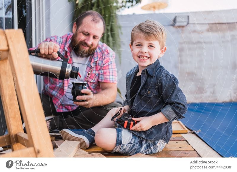 Vater serviert Kumpel gegen lächelnden Sohn mit Holzklötzen eingießen Gefährte Lächeln Thermoskanne Holzarbeiten heiter achtsam diy Pause Mann Papa Glück