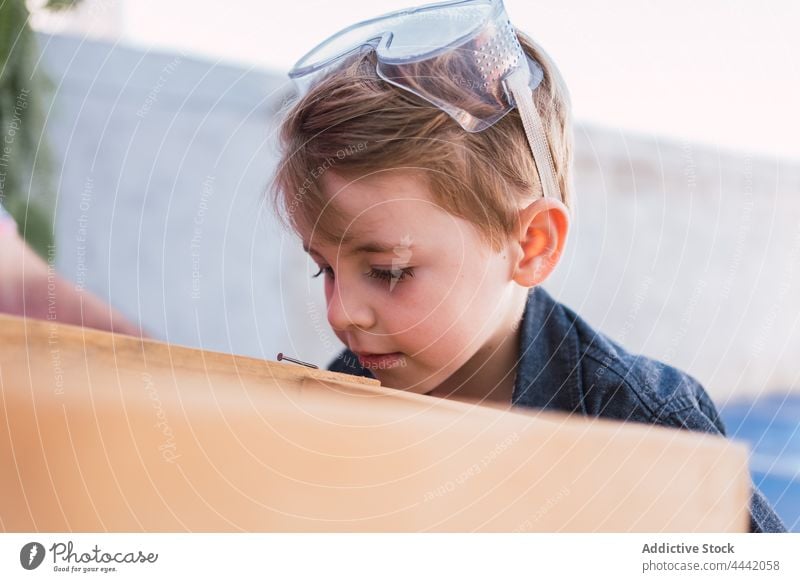 Verträumter Junge mit Schutzbrille vor einem Holzschemel Brille Sicherheit nachdenken Kindheit handgefertigt Hocker charmant Freizeit Wochenende natürlich