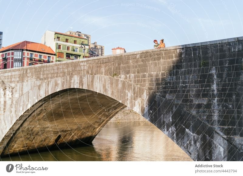 Lesbisches Paar im Gespräch auf einer alten Brücke über dem Kanal in der Stadt Architektur gewölbt lesbisch Partnerschaft reden Frauen Gebäude wolkig