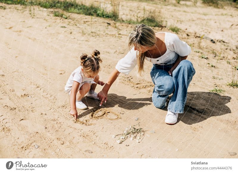 Mutter und Tochter malen gemeinsam auf dem Sand während eines Spaziergangs außerhalb der Stadt Kind Mama Glück Mädchen Familie Zeichnung Sommer Kindheit Frau