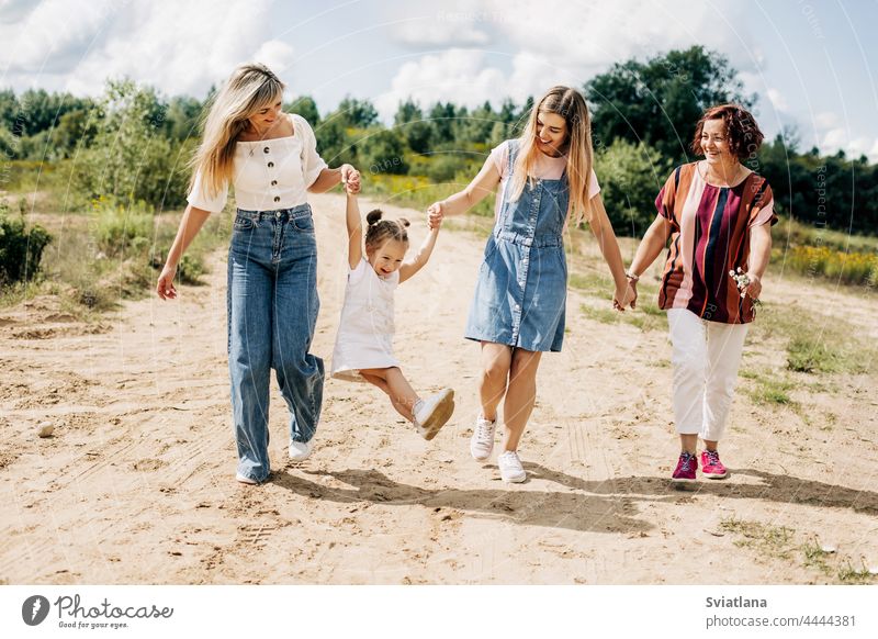 Mehrere Generationen von Frauen derselben Familie gehen auf einer unbefestigten Straße außerhalb der Stadt spazieren und genießen die gemeinsam verbrachte Zeit