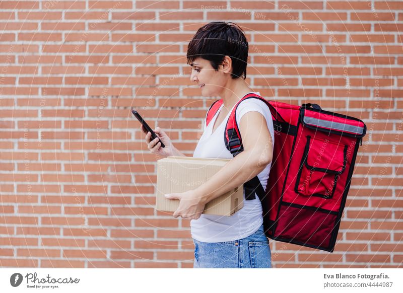 glückliche junge Reiterin mit rotem Rucksack, die eine Pappschachtel mit Lebensmitteln in der Stadt hält. Lieferservice-Konzept. Frau Überprüfung der Bestellung im Mobiltelefon