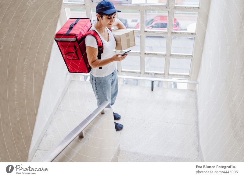 Junge Reiterin mit rotem Rucksack, die eine Pappschachtel in einer Treppe in der Nachbarschaft hält. Konzept eines Lieferdienstes. Nachhaltiger Transport Frau