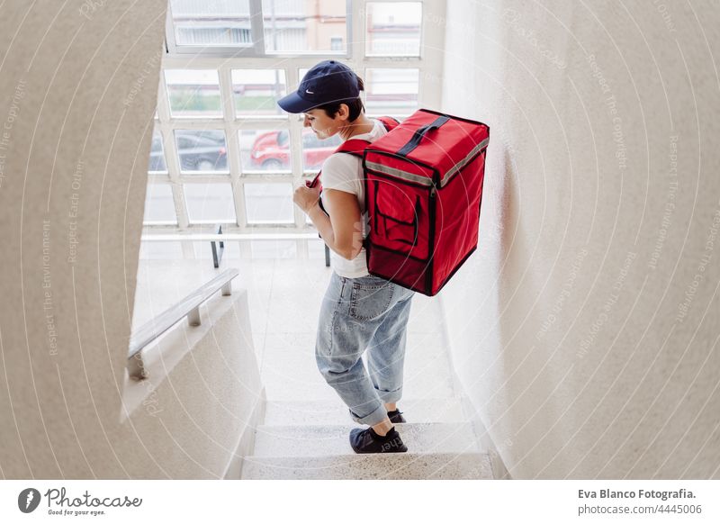 Rückenansicht der jungen Reiterin, die einen roten Rucksack trägt und eine Pappschachtel auf einer Treppe in der Nachbarschaft hält. Konzept eines Lieferdienstes. Nachhaltiger Transport