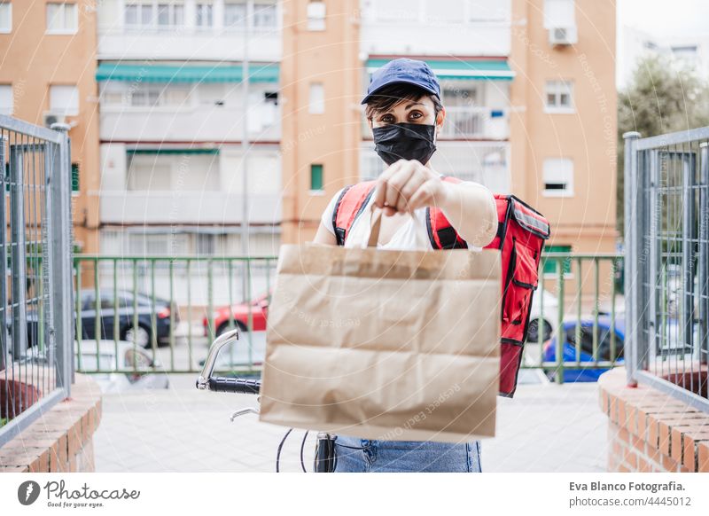 Junge Frau, die mit dem Fahrrad eine Mahlzeit ausliefert, während sie eine Maske für die Corona-Virus-Pandemie trägt. Konzept für nachhaltige und gesunde Ernährung