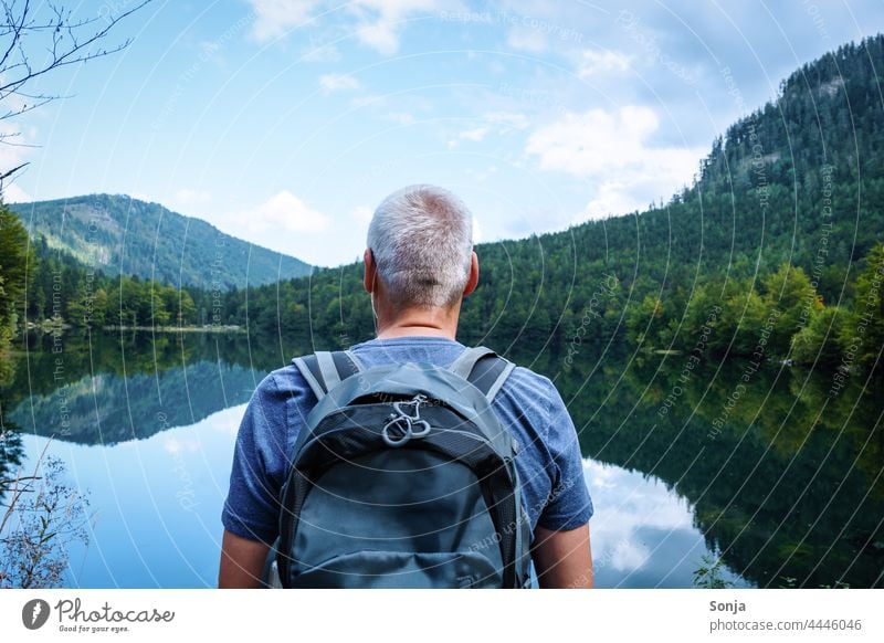 Mann mit einem Rucksack steht an einem See und genießt die Aussicht wandern Rückansicht Ausflug Tourismus Ferien & Urlaub & Reisen Freiheit Senior graue Haare