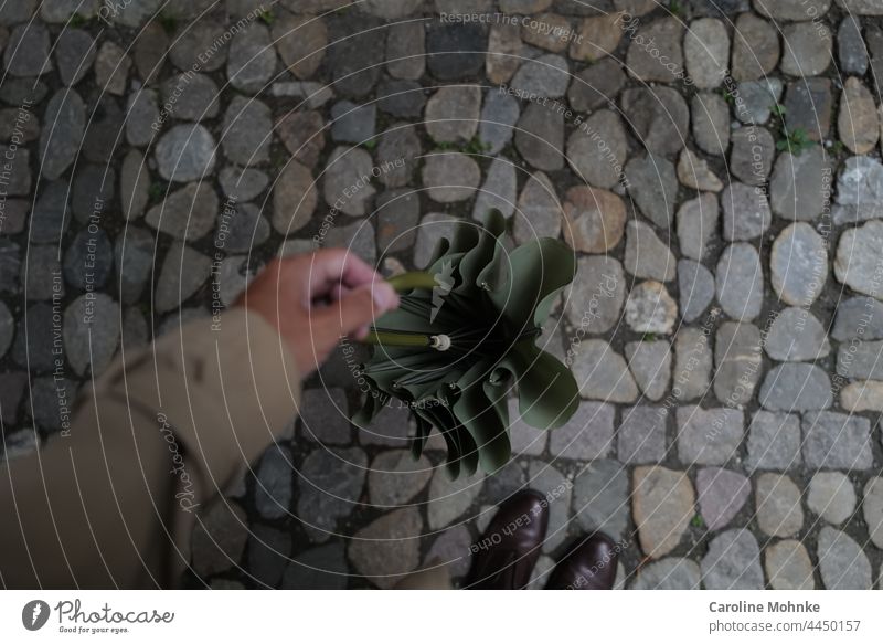 Frau hält einen grünen, alten Schirm in der Hand und blickt auf Kopfsteinpflaster Retro Regenschirm Wetter schlechtes Wetter nass Außenaufnahme Farbfoto Tag