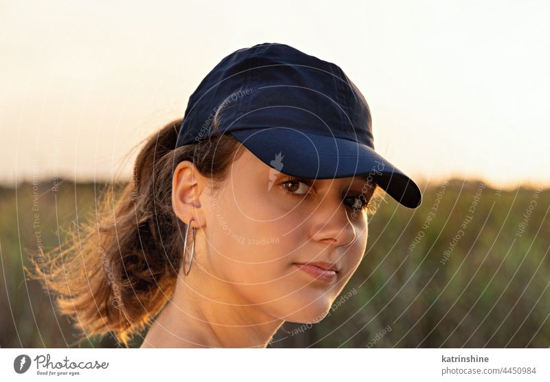 Teenager-Mädchen mit dunkelblauer Baseballmütze bei Sonnenuntergang im Freien Jugendlicher Kaukasier Attrappe visier Kopf tragend geradeaus schauend Kindheit