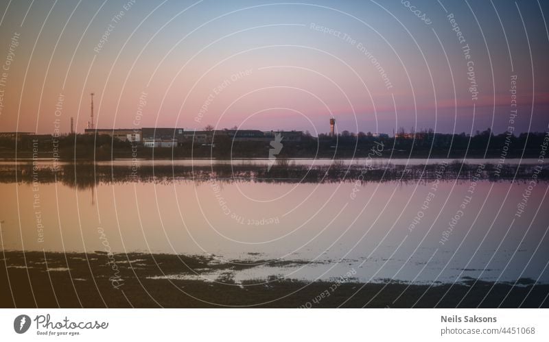 ruhiges, wellenloses Hochwasser auf einer Wiese in Lettland, schöner Frühlingsabend-Sonnenuntergang, klarer Himmel, Fabrik in der Ferne abstrakt Nachmittag