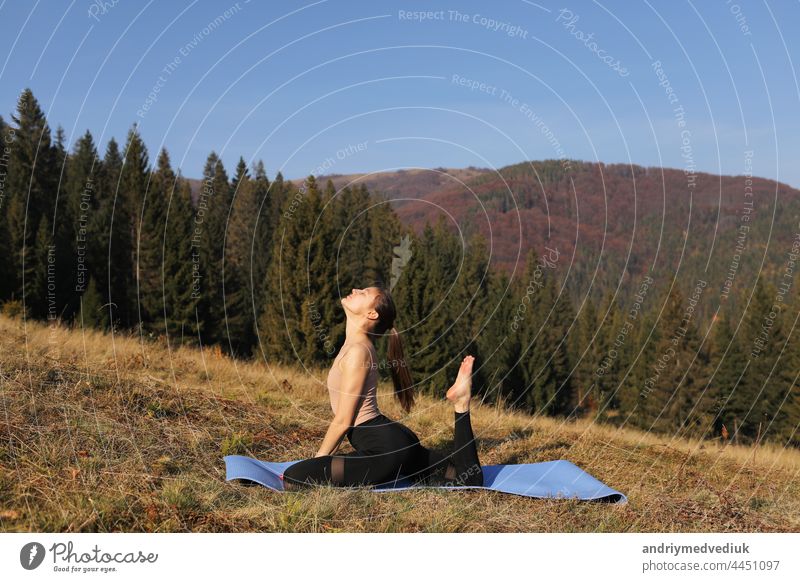 Junge fitte Frau macht Übungen auf Yoga-Matte auf dem Hintergrund der sonnigen Berge Hügel. Outdoor-Workout, gesunder Lebensstil. Frau im Sportanzug dehnt sich in der Natur gegen den Wald am Morgen