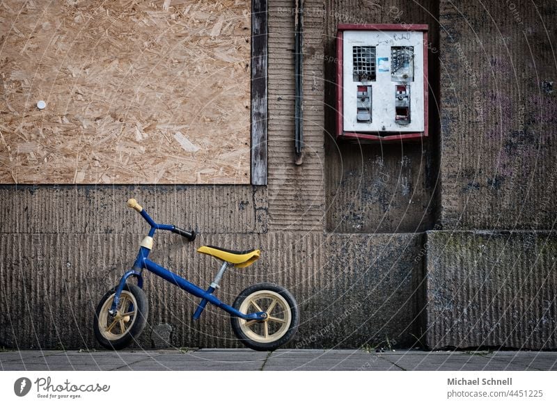 Kinderlaufrad und defekter Kaugummiautomat an einer alten, braunen Hauswand Kinderrad Laufrad Kindheit Kaugummikasten Automat Nostalgie Wand früher Erinnerung