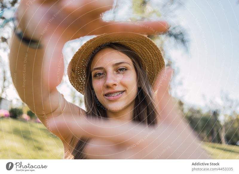 Teenager zeigt Rahmengesten im Sommerpark Foto Perspektive Bild Lächeln Klammer herzlich Park Porträt freundlich Strohhut Kleidungsstück Fotografie