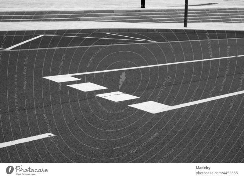 Weiße Fahrbahnmarkierungen auf dunklem Asphalt mit Abbiegespur und Bushaltestelle am Leitz-Park in Wetzlar an der Lahn in Hessen, fotografiert in klassischem Schwarzweiß