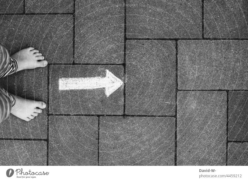 Füße eines Kindes vor einem Pfeil aus Kreide auf dem Boden der nach vorne zeigt Richtung richtungweisend geradeaus Weg Wegweiser Zukunft vorwärts Orientierung