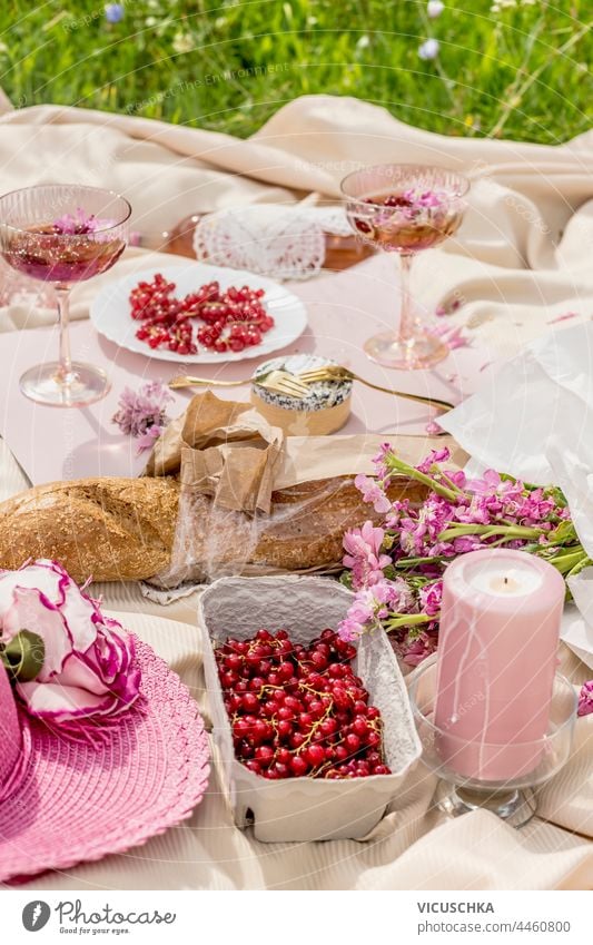 Ästhetisches Picknick mit Baguette, Sektgläsern, Beeren, Käse, Kerzen und rosa Blumenstrauß auf beiger Decke. Draußen Ästhetik Brille Champagne Haufen im Freien