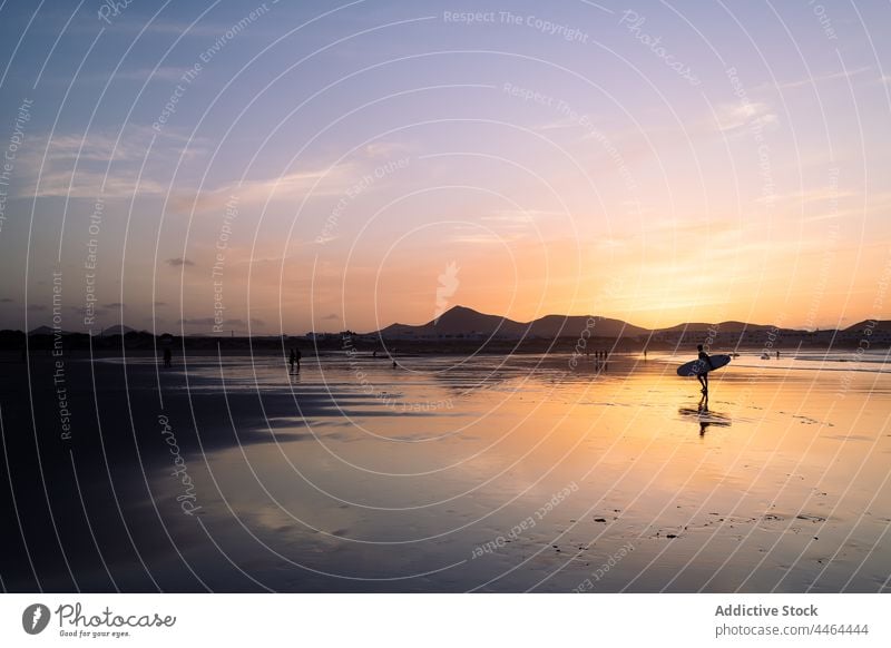 Unbekannter Surfer mit Surfbrett im Meer gegen Berg bei Sonnenuntergang MEER Silhouette Berge u. Gebirge Himmel Natur Landschaft Sport Surfen Surfboarderin