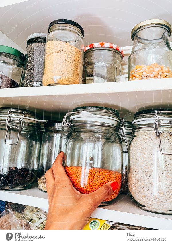 Hand greift nach einem Vorratsglas mit Linsen in einem Küchenschrank Vorratsgefäße Vorratsgläser küchenschrank rote Linse vegan Lebensmittel Vorräte