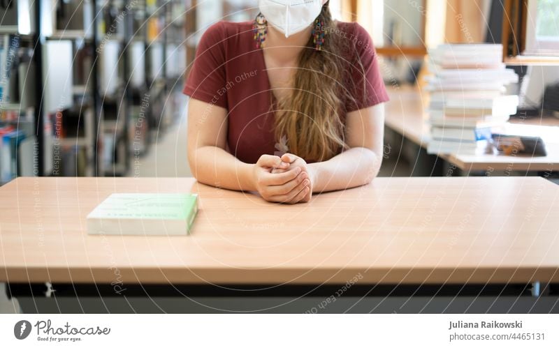 Frau sitzt am Tisch in der Bibliothek mit Maske Buch lesen lernen Bildung Wissen Studium Literatur Schule Information Weisheit Wissenschaften Bücher Sammlung