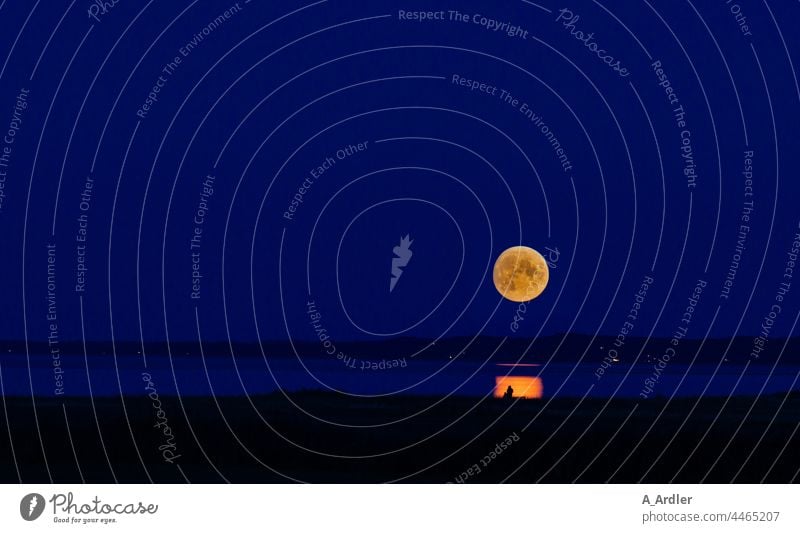 Leuchtend großer Vollmond am Himmel mit Spiegelung im Wasser, ein Liebespaar sitzt auf der Bank im Mondschein Mondaufgang Mondsüchtig Vollmondnacht