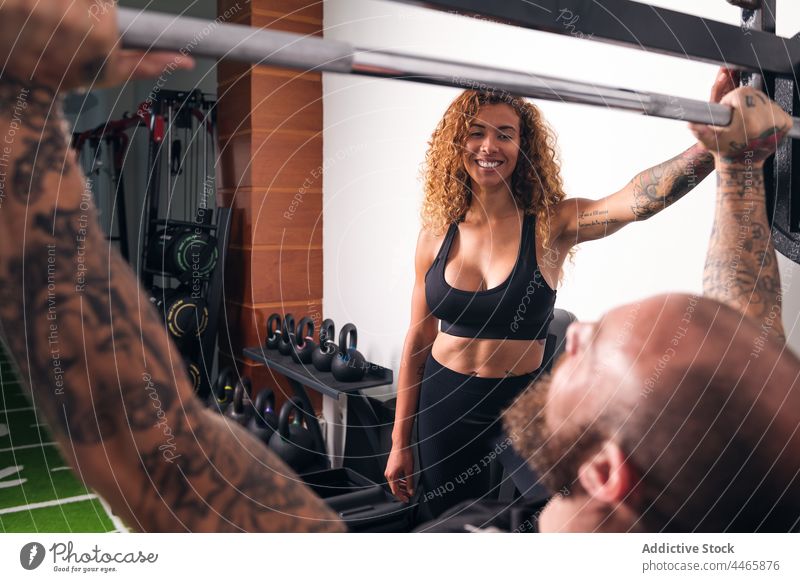 Starker Sportler bei einer Übung mit einer Langhantel im Fitnessstudio Training Gewichtheben Curl-Hantel Sportlerin hispanisch Mischrennen Ausbilderin Frau